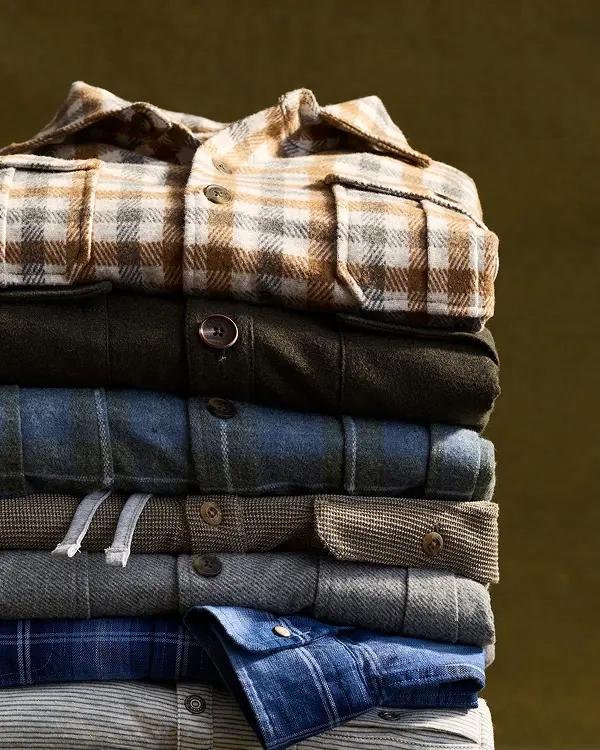 A folded stack of Lodge Shirts in plaid, charcoal, denim blue and herringbone