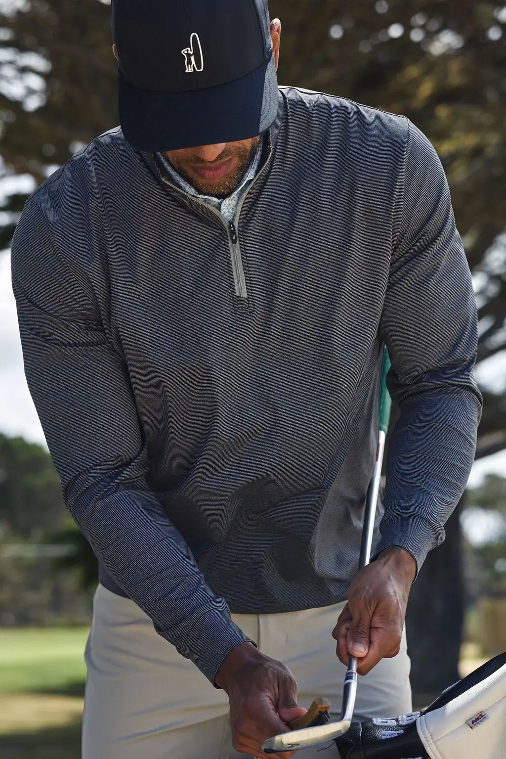 Golfer in a navy striped quarter-zip and Johnnie-O cap gripping a club, seen from above