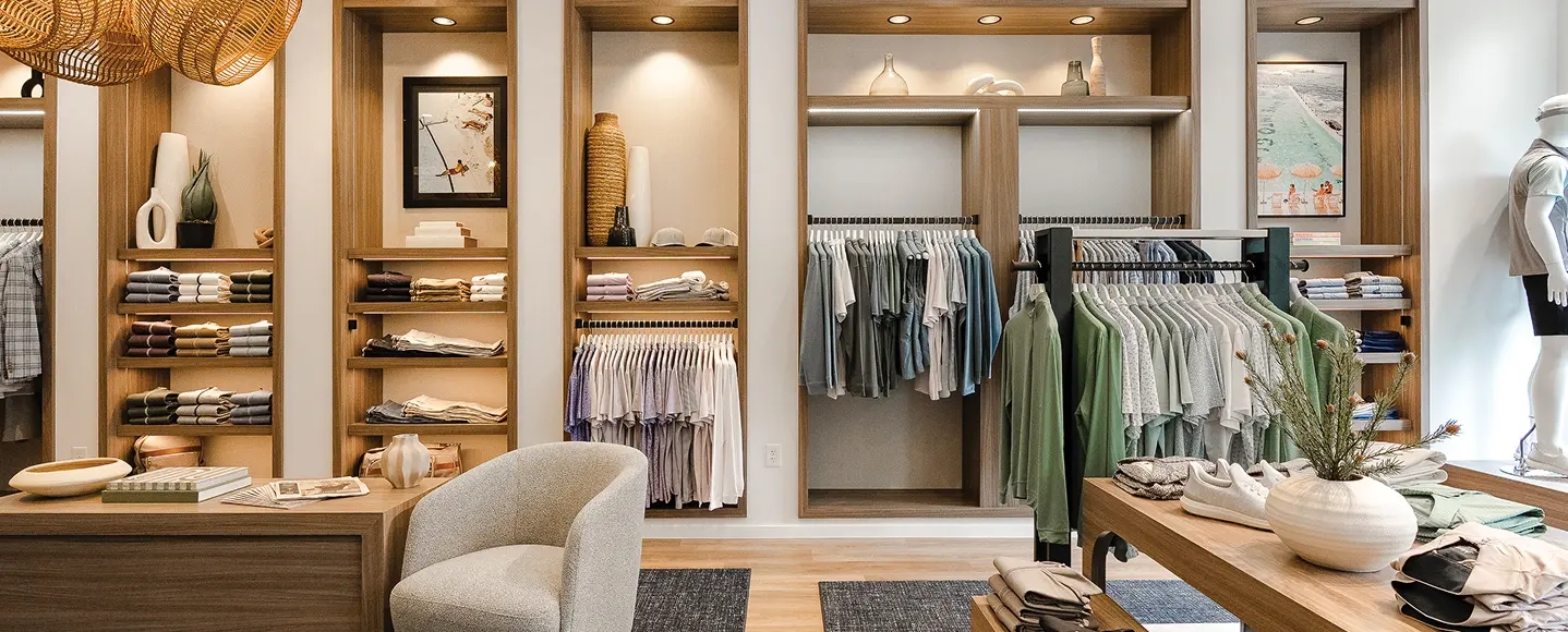 A Johnnie-O store with oak shelving, racks of polos and jackets, a boucle armchair and a table of folded shirts