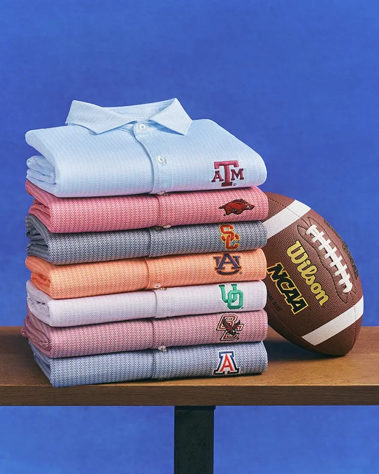 A stack of folded collegiate polos in pastel colors beside a football on a table