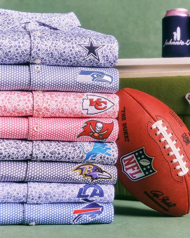 A stack of folded printed polos with pro football team logos next to a football